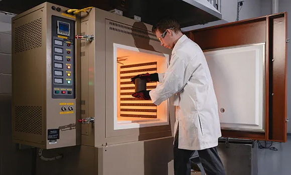 Matthew Thompson, a materials engineering doctoral candidate, loads a crucible into a box furnace to heat and remove binders from additively manufactured ceramic samples (Courtesy University photo/Charles Jischke)
