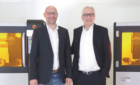 Johannes Homa, CEO of Lithoz, (left) and Volker Steinbach, CEO of Steinbach AG, with the two CeraFab S65 ceramic Additive Manufacturing machines (Courtesy Lithoz)